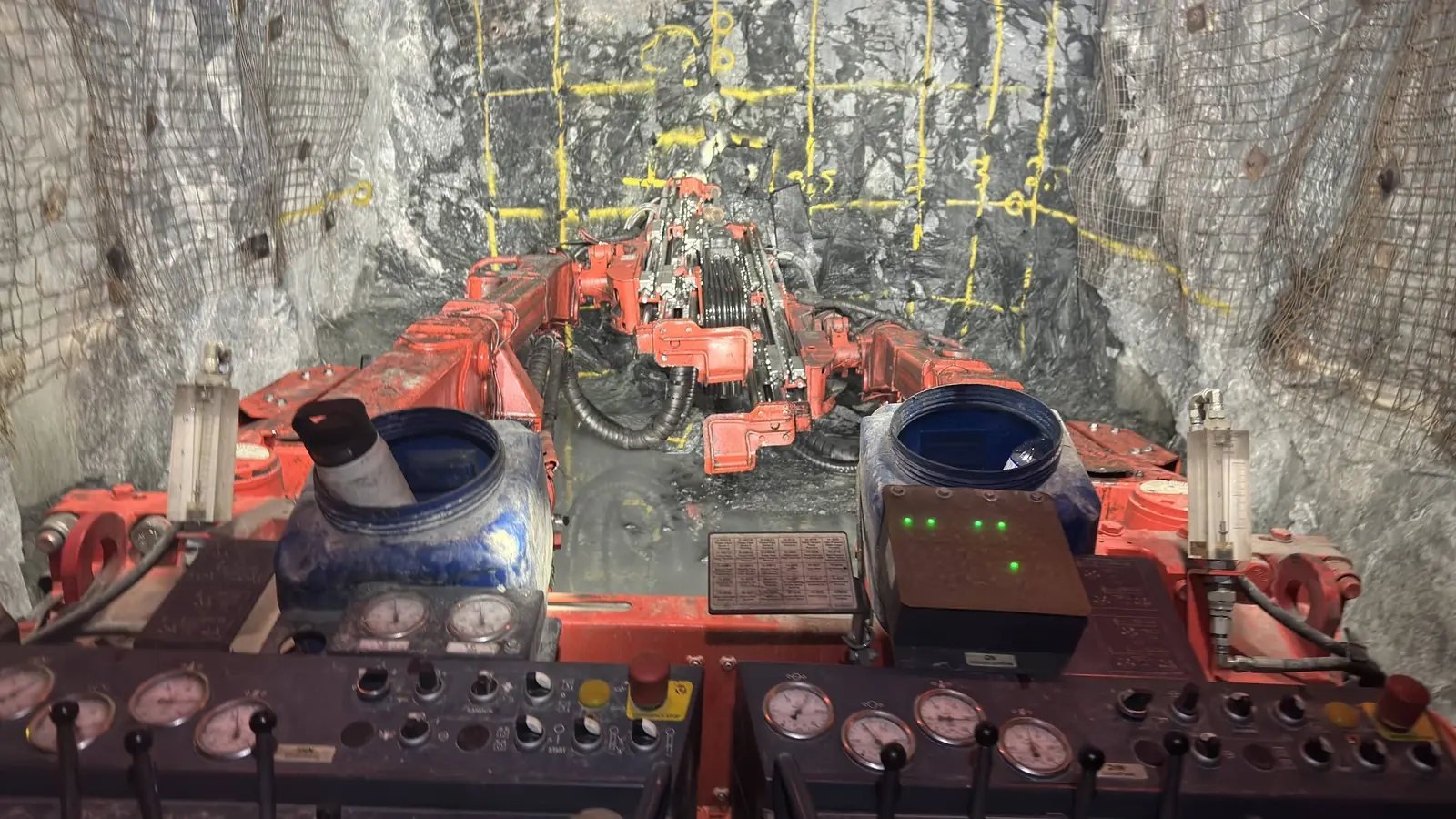 A twin-boom development jumbo at the face, seen from the operator's seat, with the drill grid painted on the rock in yellow.
