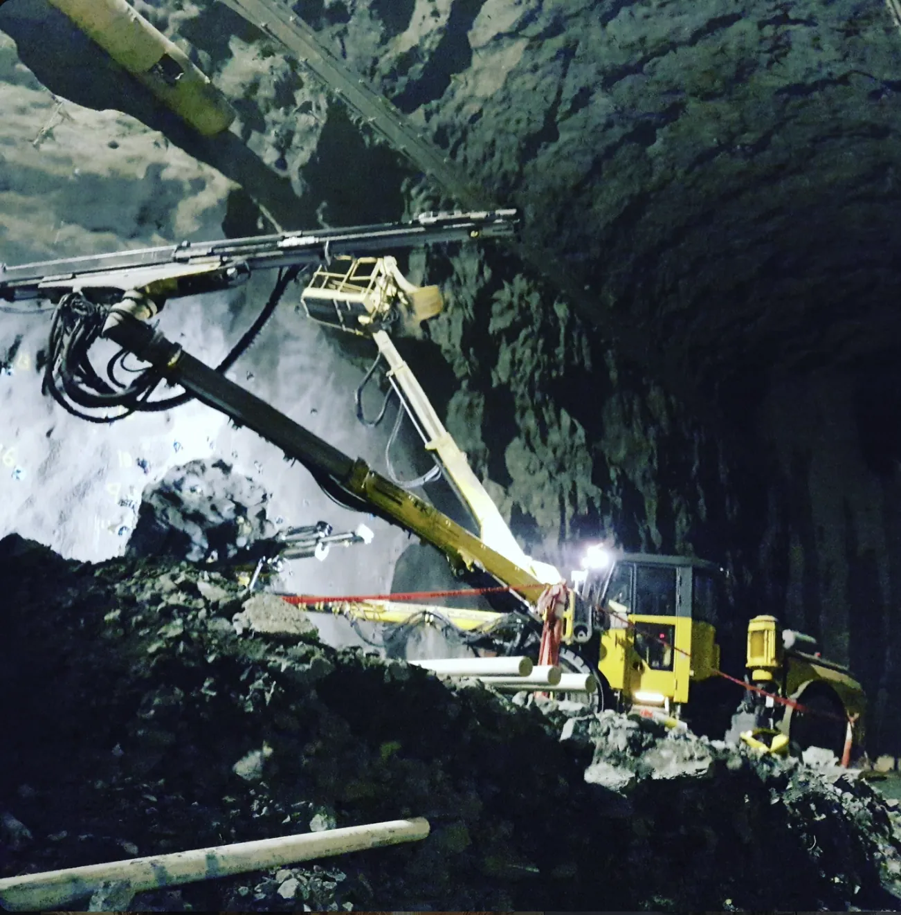 A yellow jumbo drilling over a muck pile in a large heading.